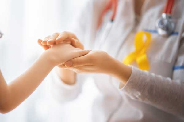 International Childhood Cancer Day. Cancer doctor in white coat with yellow ribbon holding a child's hand