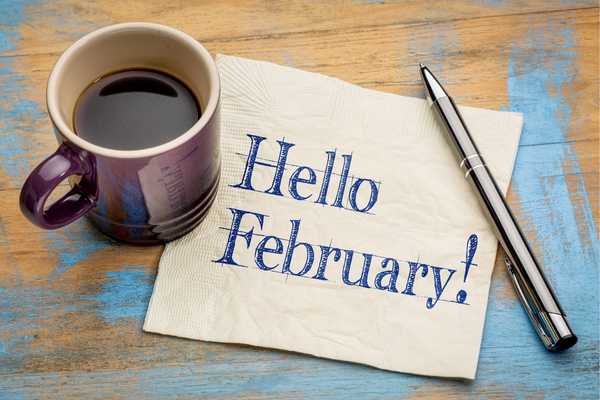 Hello February. Post it note on table that says Hello February with a pen and cup of coffee beside it