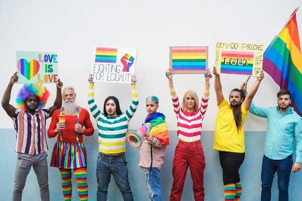 LBGT History Month. Men and women in brightly coloured clothes holding rainbow signs and flags above their heads