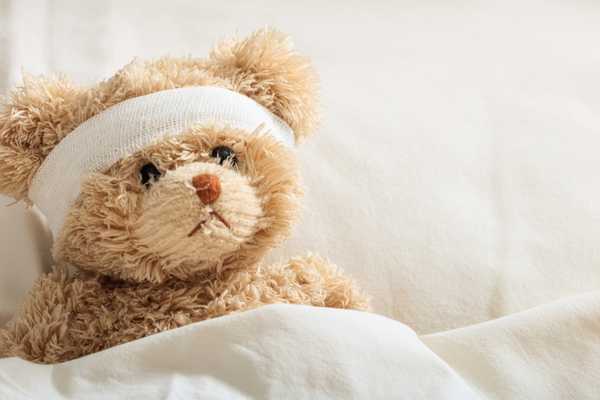 National Sickie Day. Sad teddy bear lying in bed with bandage around his head