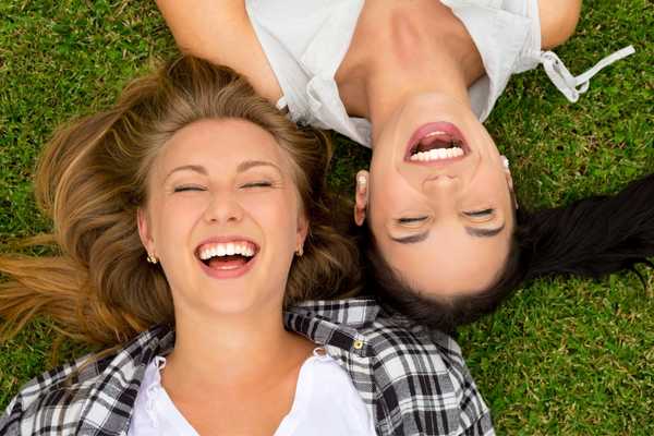 Two friends lying on grass laughing for National Best Friends Day