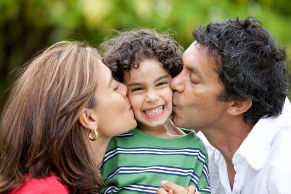 Parents either side of a child kissing them on the cheek for Global Day of Parents