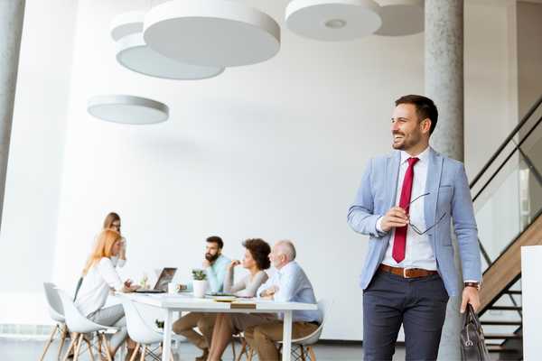 Person leaving the office with people at a desk in the background for Leave the Office Early Day