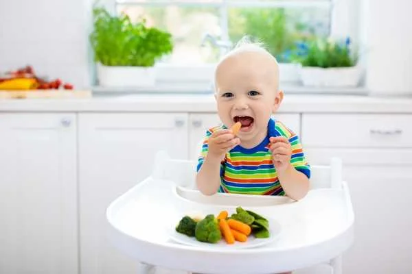 Baby feeding itself in a high chair for National Weaning Week