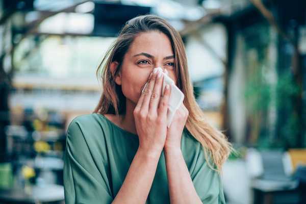 A lady sneezing into a tissue for World Allergy Week