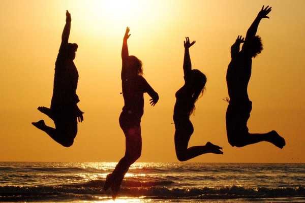 Four people jumping up in the air on a beach against an orange sunset for International Day of Happiness