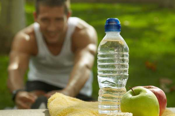 Man in background working out with a bottle of water and fruit in the foreground for Nutrition and Hydration Week