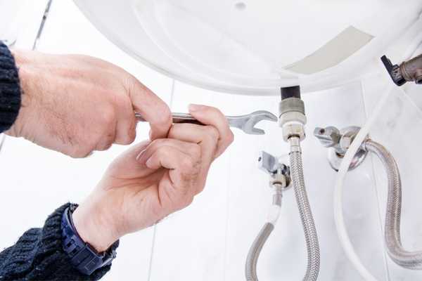 Person fixing piping underneath a sink for World Plumbing Day