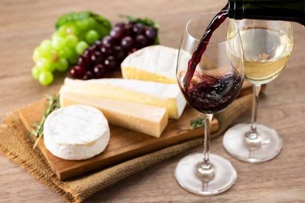 Board with a selection of cheeses and two glasses with red wine in them for National Cheese and Wine Day
