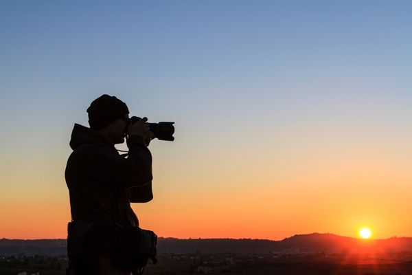 Man taking photo with a camera against a sunset for National Photography Month
