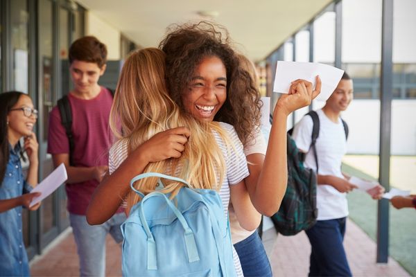 Students hugging each other in a school corridor with exam results in hand for A-Level Results