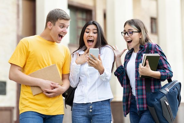 Three students with surprised faces looking at a phone for GCSE Results