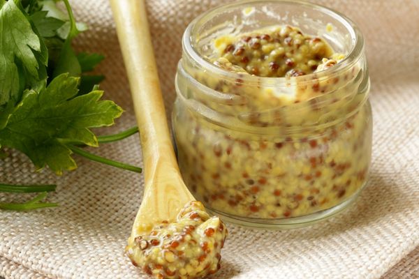 Wholegrain mustard in a jar and on a spoon for Mustard Day