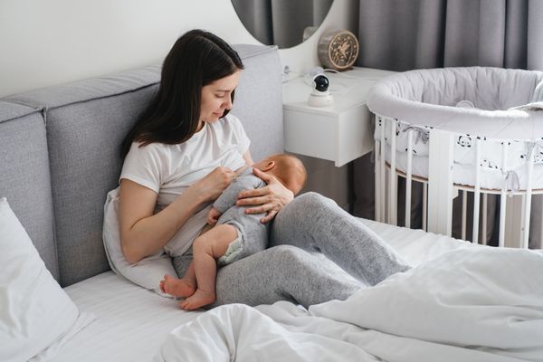 Lady breast feeding her baby sitting on a bed for World Breastfeeding Week