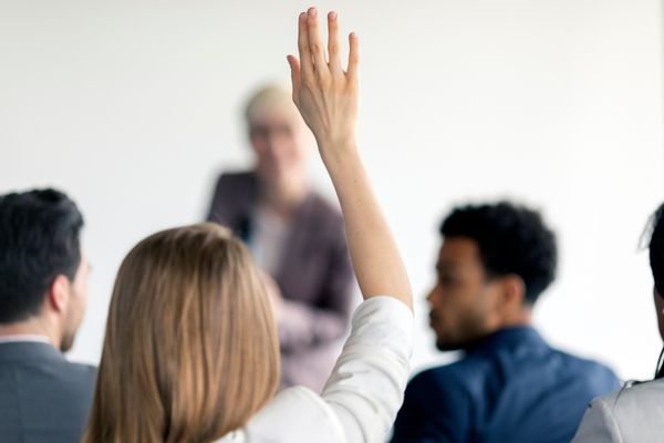 Woman raising her hand in a classroom setting for Ask a Stupid Question Day