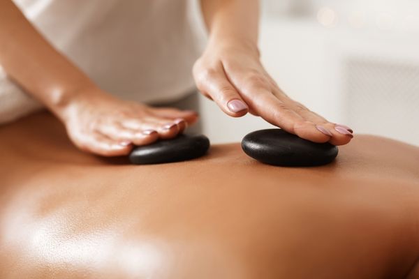 Hands massaging hot black stones into a person's back for Back Care Awareness Week