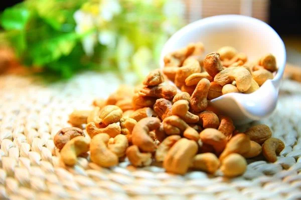 Cashew Nuts being poured out of a white bowl for Cashew Nut Day