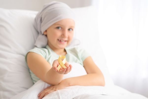 Child in hospital bed holding a yellow ribbon for Childhood Cancer Awareness Month