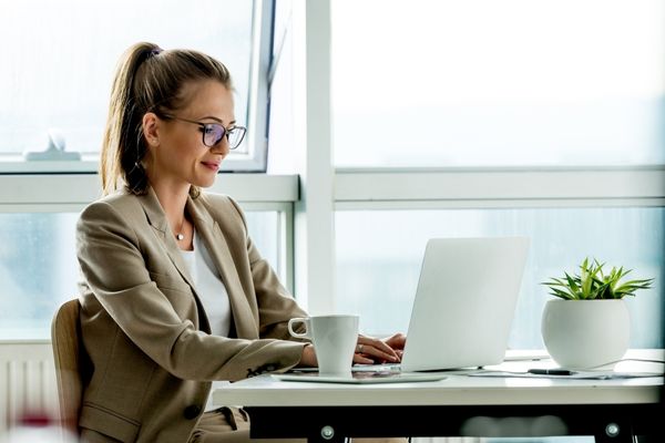 Woman sitting at a desk and typing on a white laptop for Clean Your Virtual Desktop Day