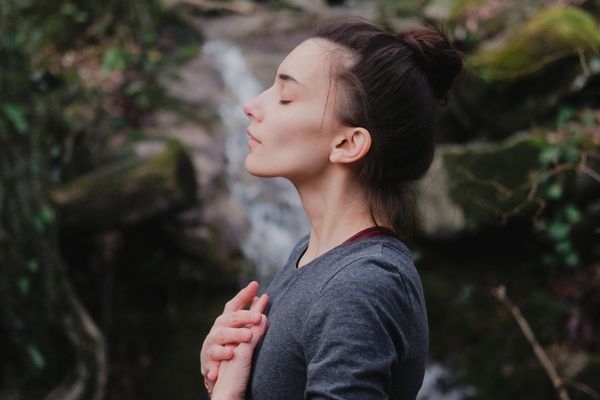 Woman with her hands on her chest and eyes closed behind a waterfall for Healthy Lung Month