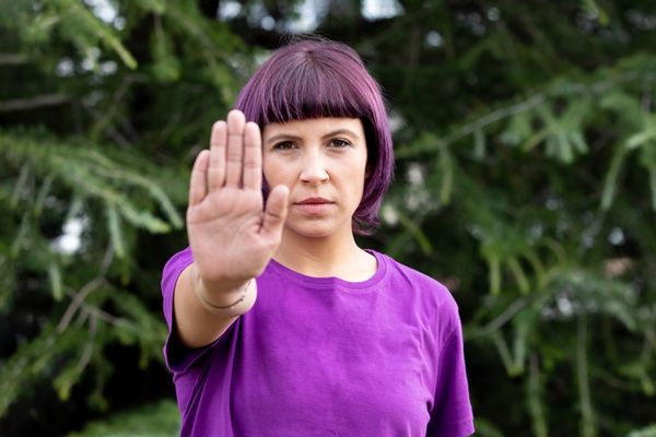 Woman in a purple top holding the palm of her hand out in front of her for International Day for the Elimination of Violence against Women