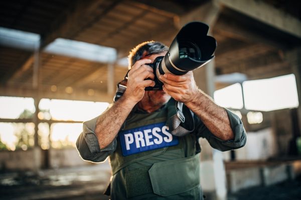 Man wearing a "press" emblazoned jacket and holding a camera for International Day to End Impunity for Crimes Against Journalists