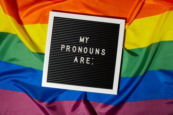 Black and white sign reading "My Pronouns Are" on a rainbow background for International Pronouns Day