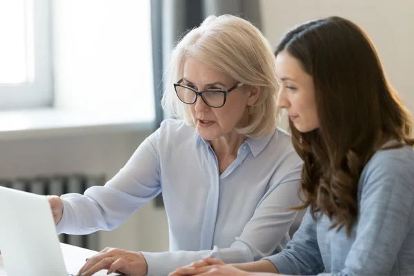 Older woman working on a computer with a younger woman for National Mentoring Day