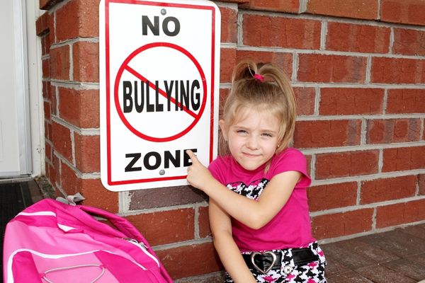Child pointing to a red and white sign reading "No Bullying Zone" for National Anti-Bullying Week