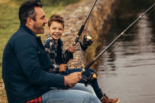 Man and boy sitting at the side of a lake fishing for National Hunting and Fishing Day