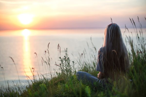 Women sitting cross-legged on grass overlooking a sunset for National Quiet Day