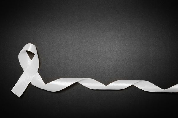 A curled white ribbon against a black background for White RIbbon Day