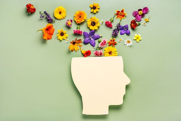 A paper cut out of a person's side profile. The top of the head has been cut off and replaced with colourful flowers for World Mental Health Day