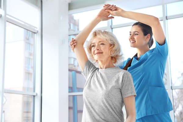 Doctor helping a woman lift her arm above her head for World Osteoporosis Day