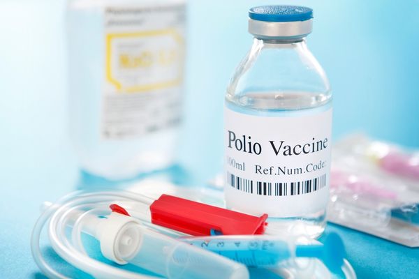 Glass bottle with sticker reading "Polio Vaccine" with two syringes for World Polio Day