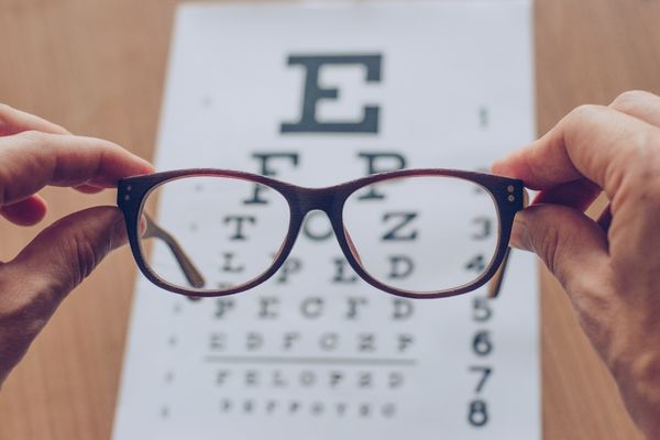 Pair of red glasses being held against a sight chart for World Sight Day