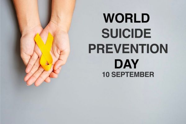 Pair of hands holding a yellow ribbon against a grey background with text reading "World Suicide Prevention Day 10th September" for World Suicide Prevention Day