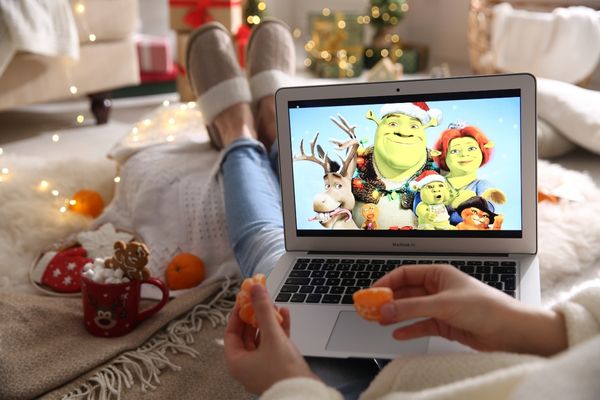 Person lying on a sofa watching a Shrek Christmas movie on a laptop for Christmas Movie Marathon Day