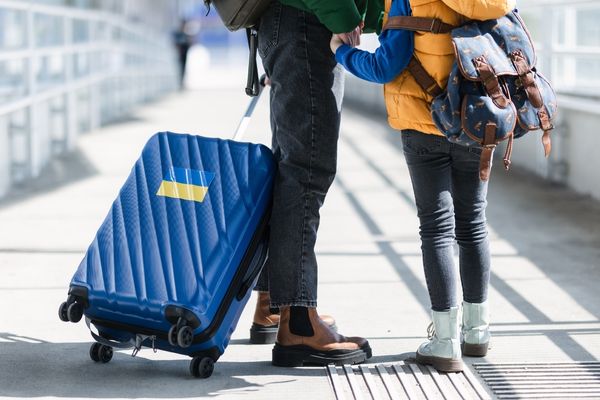 Two people wheeling a suitcase for International Migrants Day