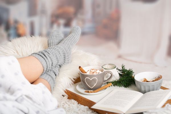 Person lying on a bed with an open book and a cup of coffee for Twixmas