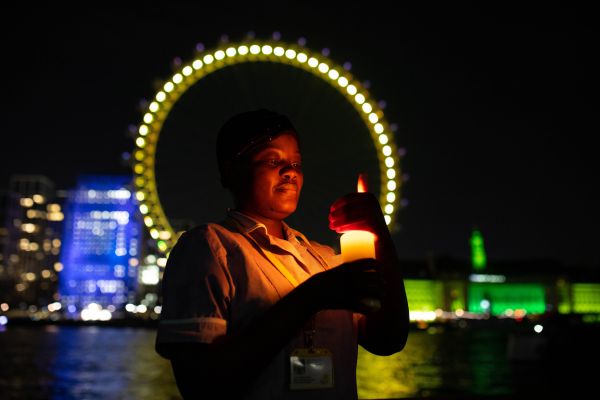 Marie Curie nurse holding a candle in the dark in front of the illuminated London eye.
