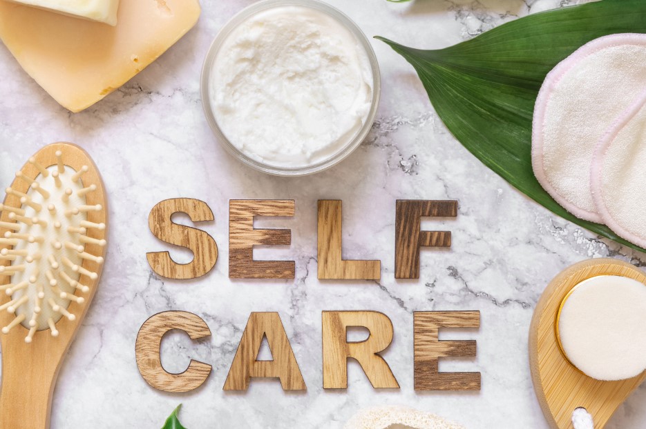 Cream, brush, and SELF CARE written on a white towel for Intl Self-Care day