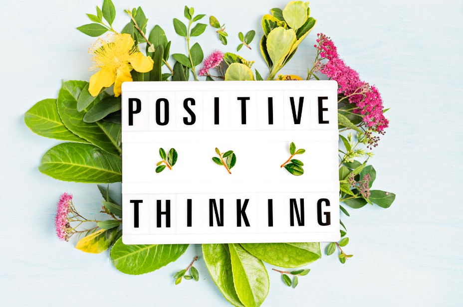 A sign saying Positive Thinking sitting on flowers for positive thinking day